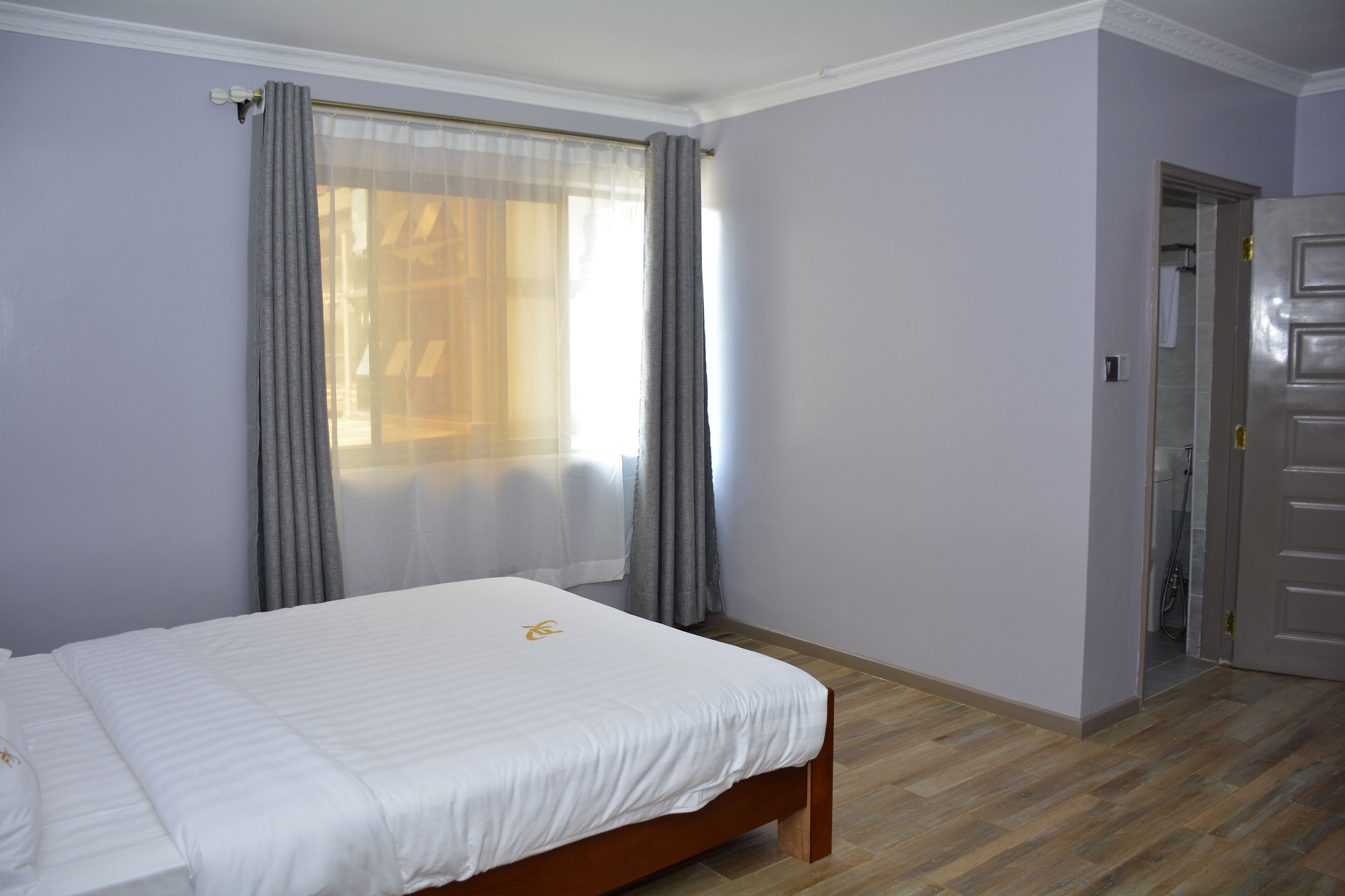 A bedroom with a bed, a window with curtains, a door, and a wooden floor.