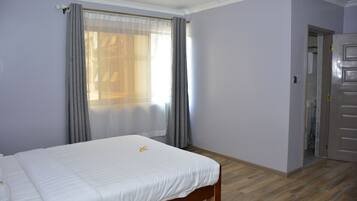 A bedroom with a bed, a window with curtains, a door, and a wooden floor.