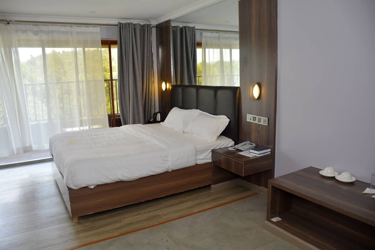 Ein modernes Hotelzimmer mit einem Holzbett, einem Nachttisch mit Lampe und Blick ins Freie durch große Fenster.