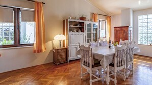 A dining area with a wooden herringbone floor, a white table with chairs, a cabinet with glass doors, and a hanging light fixture.