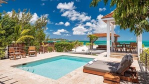 Zona de piscina con sillones de descanso, un pequeño pabellón y vista al océano.
