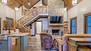 Un vaste espace de vie agrémenté d’une cheminée en pierre, d’un escalier en bois et d’un grand îlot central doté d’un évier.