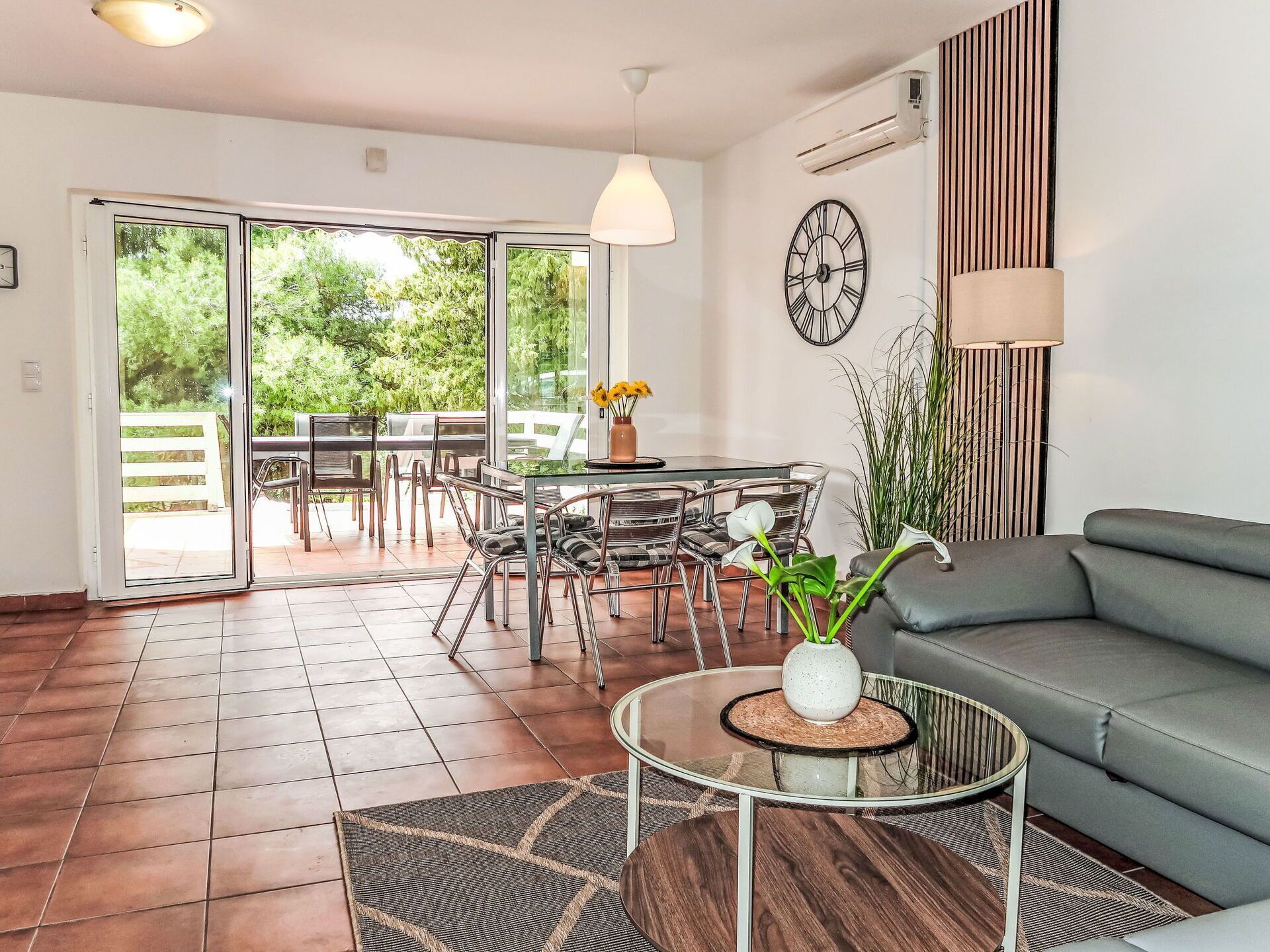 A modern living room with a glass coffee table, a grey sofa, and a dining area with a glass table and chairs.