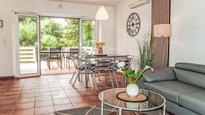 Un salon moderne avec une table basse en verre, un canapé gris et un coin repas comprenant une table et des chaises en verre.