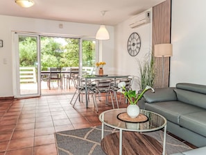 Un moderno salón con una mesa de vidrio, sofá gris y vistas al exterior.