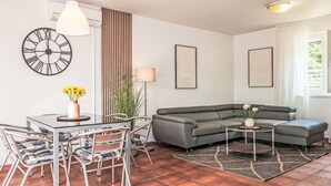 Un salon moderne avec une table à manger en verre, un canapé gris et une horloge décorative au mur.