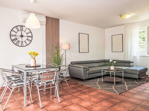 A modern living room with a glass dining table, grey sofa, and a decorative clock on the wall.