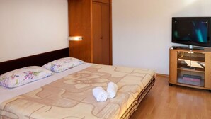 Quarto de hotel com uma cama, guarda-roupa de madeira, uma televisão e um pequeno armário de madeira.