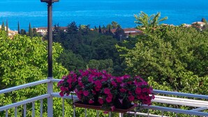 Varanda com um vaso de flores pendurado e um lampião, com vista para a costa, casas e árvores.