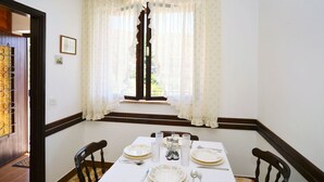 Uma sala de jantar com uma mesa posta para quatro pessoas, com toalhas de mesa floridas, pratos, talheres e copos.