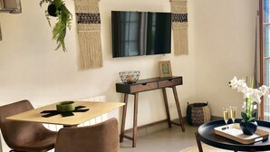 A dining area with a wooden table, brown chairs, a TV mounted on the wall, and decorative wall hangings.
