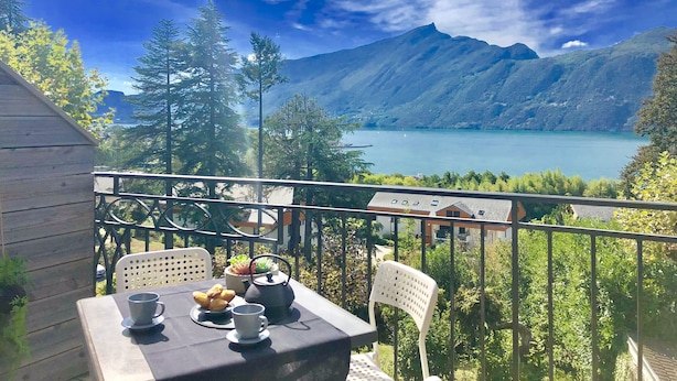 A balcony with a table set for breakfast, overlooking a lake and mountains.