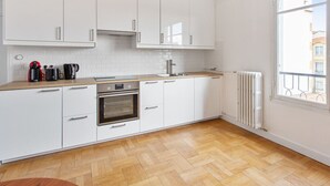 Une cuisine moderne avec des armoires blanches, un plan de travail en bois, un four encastré et une fenêtre donnant sur des immeubles.