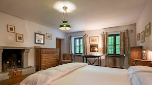 A bedroom with a large bed, a dresser, a chair, a table, a fireplace, and a window with curtains. - Wonderful private villa for 12 guests with WIFI, private pool, TV, terrace and pets allowed (Valfenera)
