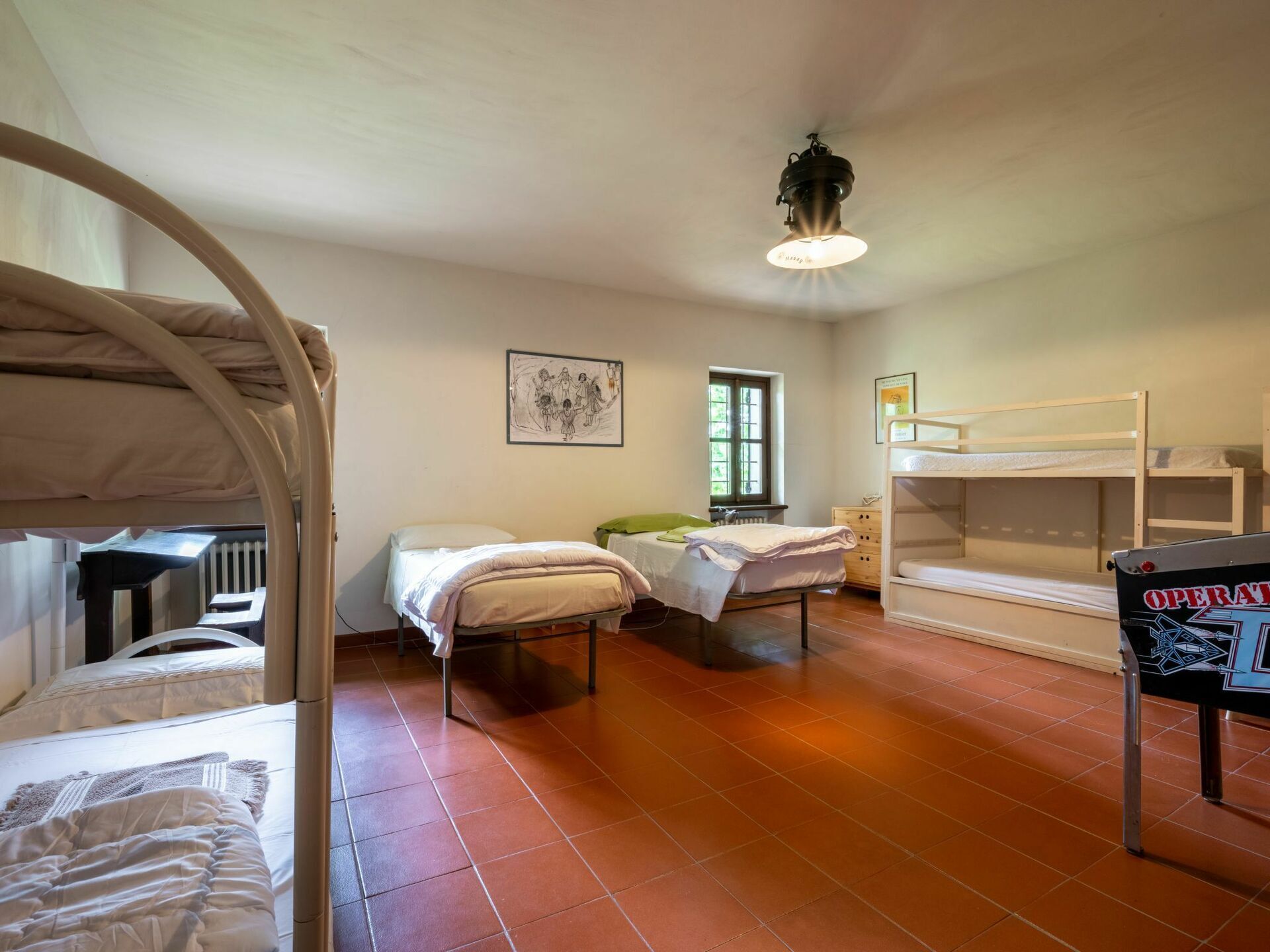 A dormitory room with bunk beds, a single bed, a desk, and a window.