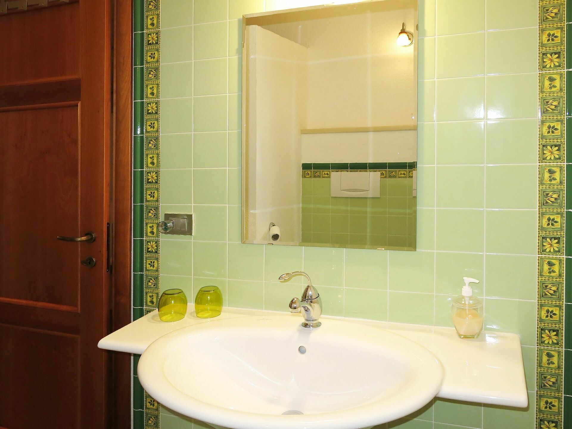 Un baño con un lavabo blanco, un espejo y baldosas verdes con diseño.