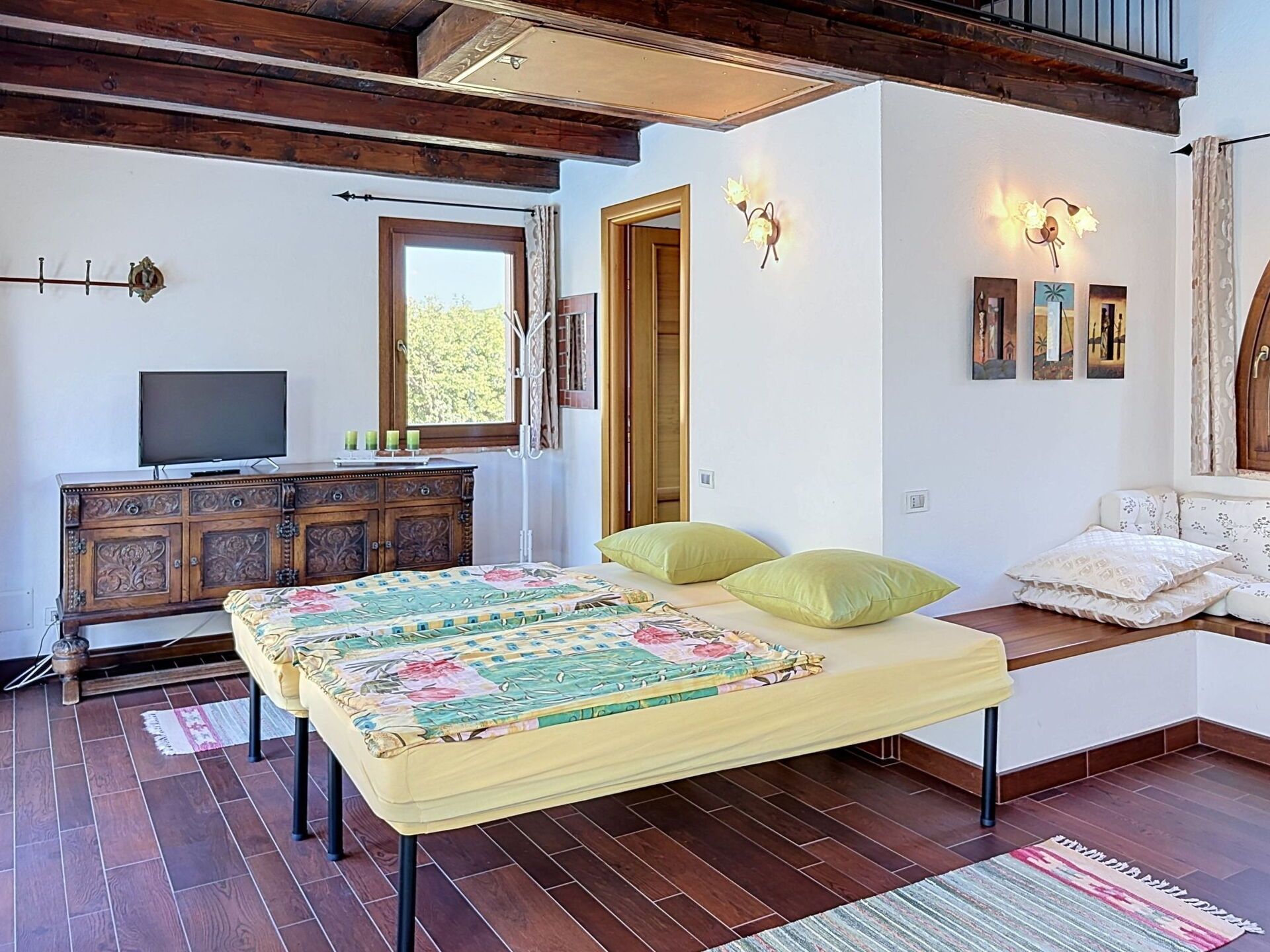 Un dormitorio con cama, televisor, cómoda de madera y ventana.