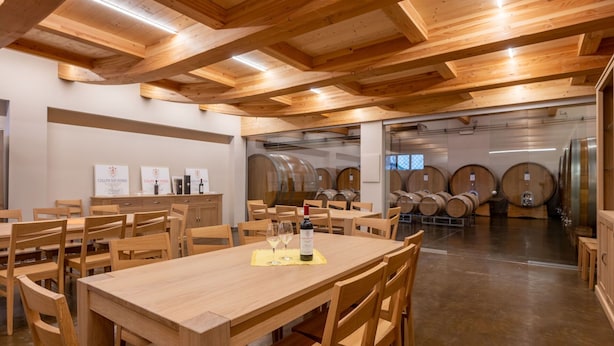 Een restaurant met houten tafels en stoelen, een wijnrek op de achtergrond en een modern plafondontwerp.