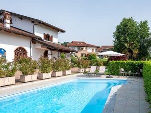 A swimming pool with a tiled deck, surrounded by potted plants and outdoor furniture.