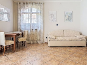 A living room with a sofa, a dining table with chairs, a window with curtains, and two wall-mounted artworks. - Beautiful  villa for 6 guests with WIFI, TV and terrace (Barolo)
