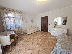 Un dormitorio con cama, sofá, escritorio, silla, cómoda, puerta y ventana con cortinas.