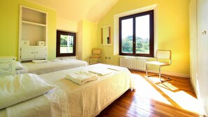 A bright room with two beds, a chair, and a window with a view of greenery.