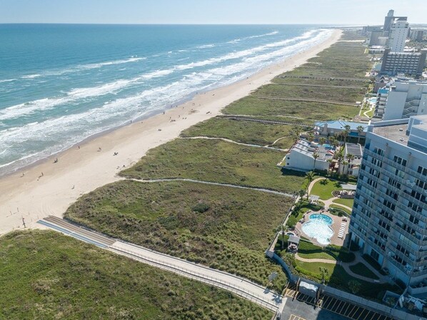 An aerial view of a coastal hotel with a beach, a swimming pool, and a boardwalk.