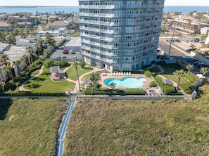 A high-rise hotel with a swimming pool, surrounded by greenery and a parking area.