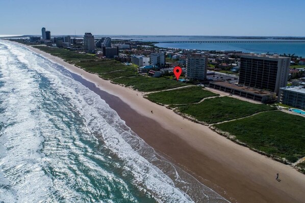An aerial view of a coastal city with a beach, buildings, and a bridge in the distance.