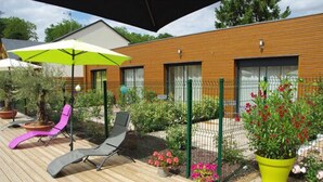A wooden deck with two lounge chairs, a green umbrella, and potted plants. - Les Abris du Chateau (Mer)