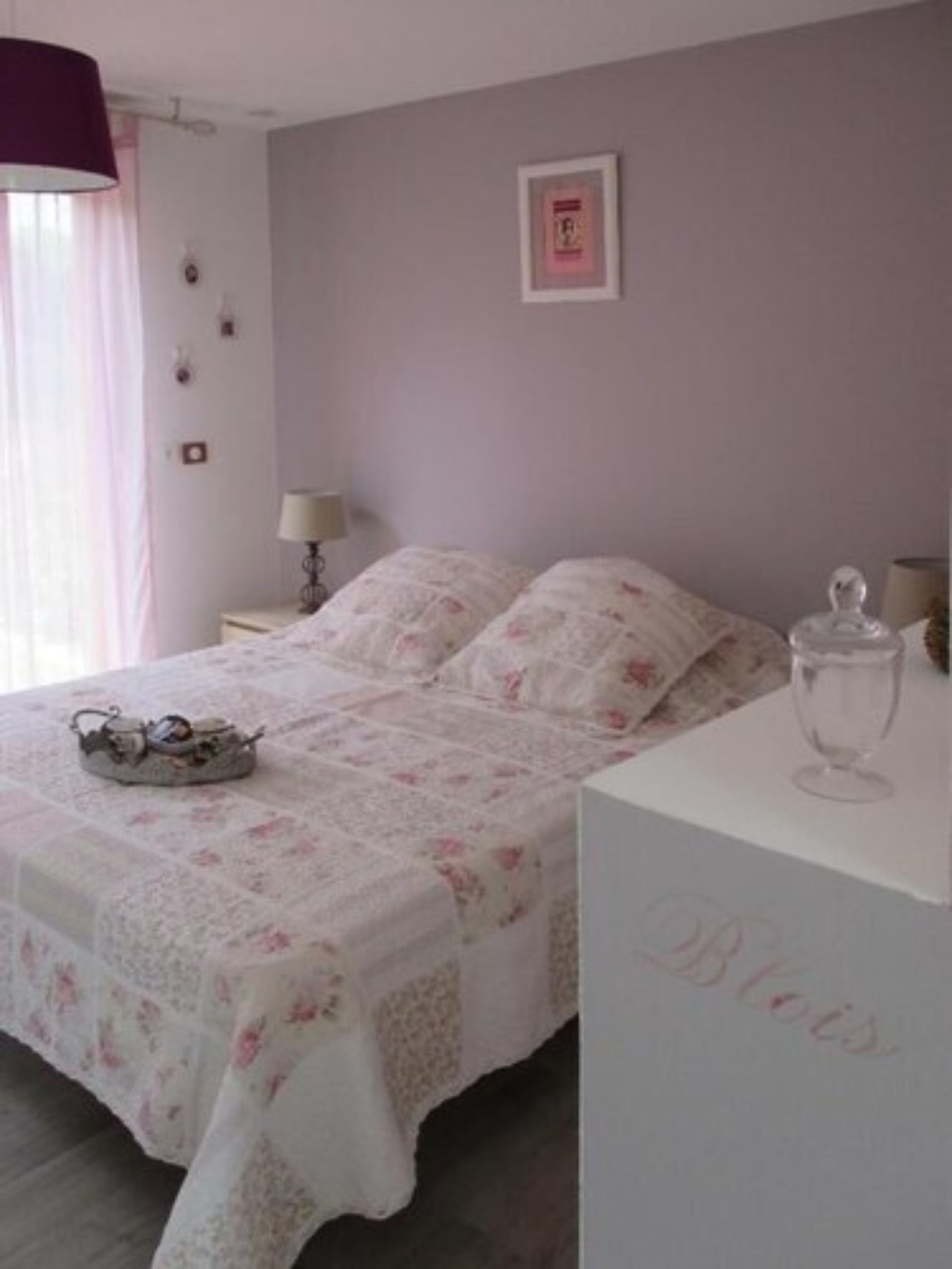 A bedroom with a bed, a nightstand, a lamp, and a dresser.
