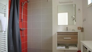 A bathroom with a shower, a sink with a mirror, and a towel rack. - Les Abris du Chateau (Mer)