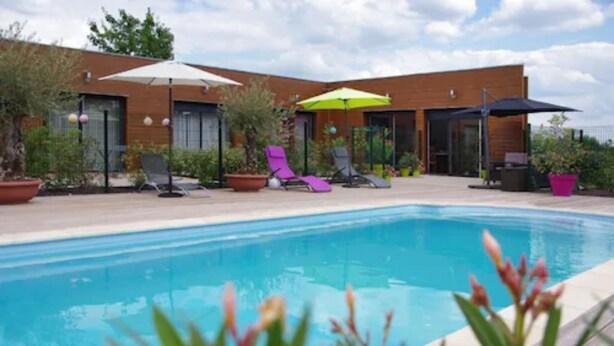 A swimming pool with lounge chairs and umbrellas, surrounded by potted plants and a modern building with large windows. - Les Abris du Chateau (Mer)