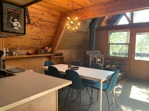 L’intérieur chaleureux d’un chalet, avec un revêtement mural en bois, un coin repas avec des chaises bleues, une cuisine équipée d’une cuisinière et une affiche encadrée accrochée au mur.