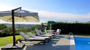 A poolside area with lounge chairs and umbrellas, a pool, and a view of the landscape. - Stunning private villa for 10 guests with WIFI, private pool, TV, terrace and pets allowed (Capriglio)