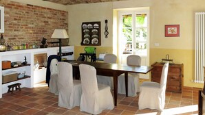 A dining area with a brick wall, a wooden table, and chairs. There is a window with a view of greenery outside. - Stunning private villa for 10 guests with WIFI, private pool, TV, terrace and pets allowed (Capriglio)