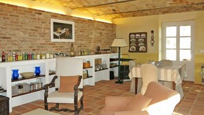 A cozy living room with a brick wall, a dining area with a table and chairs, and a shelf with various bottles and glasses. - Stunning private villa for 10 guests with WIFI, private pool, TV, terrace and pets allowed (Capriglio)