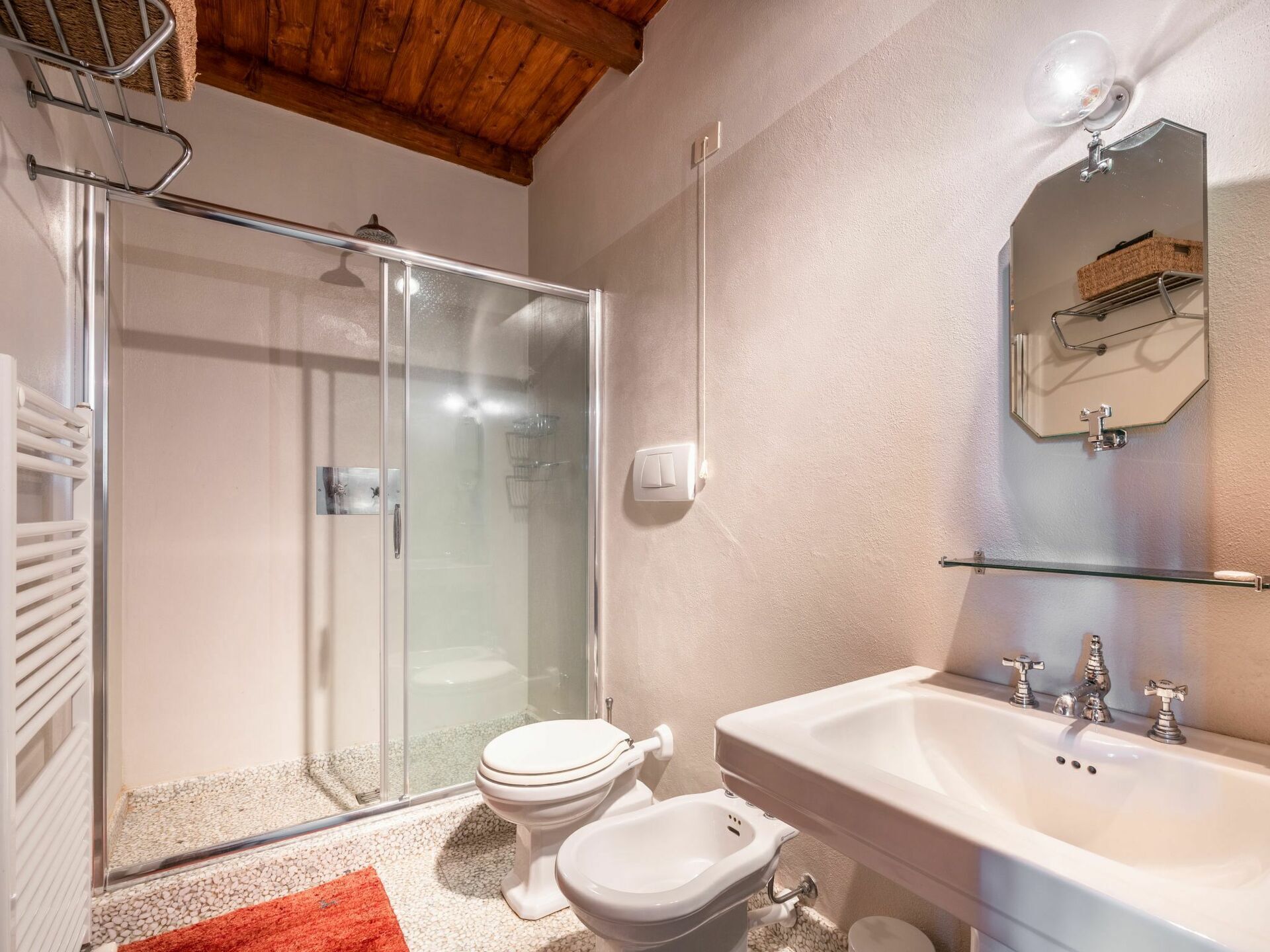 A bathroom with a glass-enclosed shower, a white sink with two faucets, and a toilet.