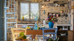 Una cocina rústica con pared de piedra, una mesa de madera, sillas y un florero azul con flores.