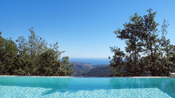 Una piscina infinita con agua azul cristalina y vistas al océano y colinas de fondo.