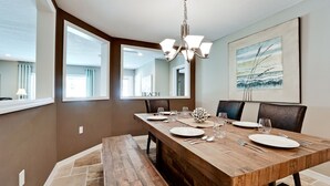 A dining room with a wooden table set for six, large windows, a chandelier, and a beach-themed painting. - Tropical Highlands - 6 BEDROOMS/3 Bathroom/2 King Masters/3800 sf/Large Htd Pool (Bradenton)