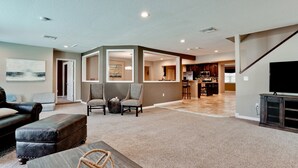 A spacious living room with a large sectional sofa, two armchairs, and a coffee table. A kitchen area is visible in the background with a dining table and chairs. - Tropical Highlands - 6 BEDROOMS/3 Bathroom/2 King Masters/3800 sf/Large Htd Pool (Bradenton)