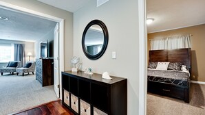 A bedroom with a bed, a dresser, a mirror, and a TV in the adjacent living area. - Tropical Highlands - 6 BEDROOMS/3 Bathroom/2 King Masters/3800 sf/Large Htd Pool (Bradenton)