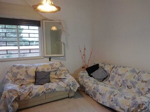 A room with two sofas covered in a patterned fabric, a window with blinds, a hanging light fixture, and a wall-mounted mirror.