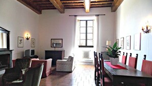 A dining area with a wooden table, chairs, a fireplace, and a large window. - Cosy apartment in villa for 8 people with WIFI, pool, TV and panoramic view (Scarperia)