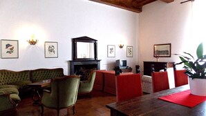 A traditional living room with a fireplace, green upholstered sofa, red chairs, and a wooden table. - Cosy apartment in villa for 8 people with WIFI, pool, TV and panoramic view (Scarperia)