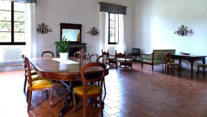 Une salle à manger spacieuse avec une grande table en bois, plusieurs chaises, une plante en pot et une cheminée.