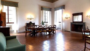 Une pièce spacieuse avec une table à manger en bois entourée de chaises, une cheminée et de grandes fenêtres avec des rideaux.