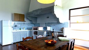 Een keuken met een eettafel, stoelen, een magnetron, een fornuis en een koelkast.