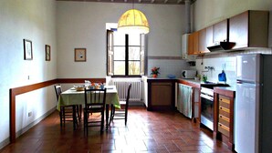 Een keuken met een eettafel, stoelen, een hanglamp, een raam en een koelkast.